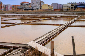 Fototapeta premium Salt evaporation ponds with wooden frames reflecting sky in Pomorie, Bulgaria, surrounded by residential buildings. Concept of traditional saltwork within modern coastal town