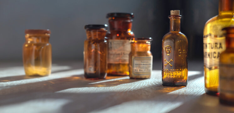 Poison bottle with skull and bones stands among pharmaceutical bottles. Danger sign, symbol of death. Concept background on poison poisoning, pharmaceutical, chemistry, medical, old science topic.