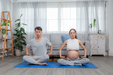 Healthy asian family sitting on yoga mat working out together in living room, Pregnancy of young woman enjoy with yoga to breathing and meditation at home,Motherhood and Wellness Pregnant Concept.