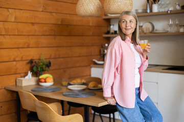 Obraz premium Friendly woman holding healthy orange juice while posing in kitchen