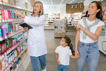 Obraz premium Pharmacist advising a young woman with a little girl on medicines