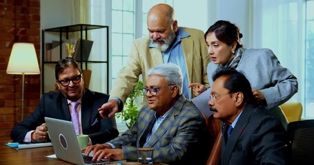 Indian five business people working on laptop as senior Indian Asian businessmen collaborate while sitting or standing at table reviewing project tasks together inside modern corporate office - Powered by Adobe