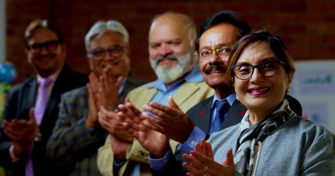 Portrait of Indian senior businesspeople clapping with smile as senior Indian Asian executives applaud and celebrate success while looking at camera inside modern corporate office workplace