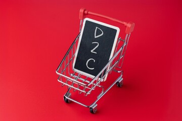 Mini shopping cart holding a chalkboard with D2C text. Direct to consumer business model, ecommerce concept.