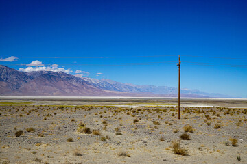 Remote desert plain with power lines and mountains on the horizon under deep blue sky. Concept of infrastructure, isolation, energy, minimalism and vast open space.