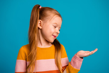 Cheerful young girl with a bright orange yellow striped sweater smiles as she presents her hand on a blue background in a playful lifestyle stock photo