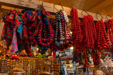 Vibrant handmade bead necklaces and traditional floral scarves hang from a wooden rack at a souvenir stall, creating a rich pattern of color and texture for holiday shopping, craft culture, and gift c