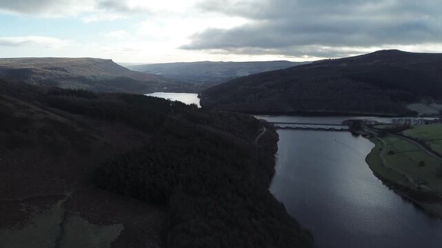 Aerial drone footage pushing forward over Ladybower Reservoir in Derbyshire, England, showing water, hills and bridge, suitable for travel, infrastructure, environment and establishing shot use.