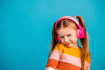 Young girl with pink headphones smiling against a bright blue background in a playful fashion portrait of childhood joy and casual style for kids