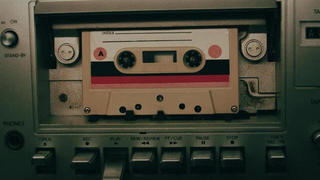 Cassette tape playing music in retro stereo player. Close-up of a plastic, audio cassette tape playing in a vintage tape deck. A music technology, video background loop.