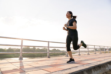 Active Asian woman running outdoors along a riverside walkway.
