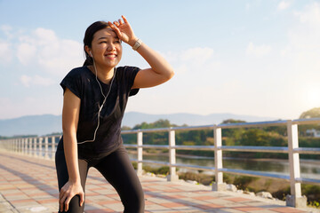 Asian woman smiling and resting after outdoor workout on a riverside path.