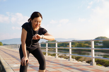 Asian woman checking smartwatch after outdoor workout on a riverside path.
