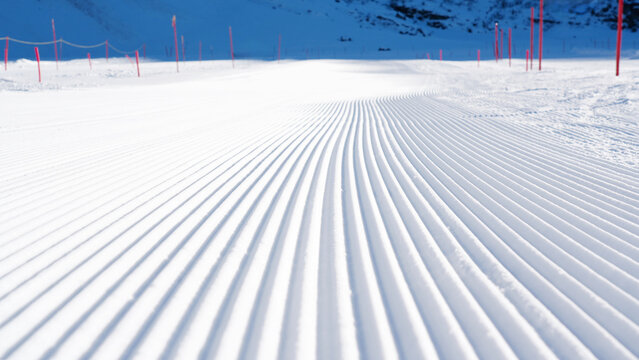 Groomed ski slope with corduroy snow texture, showcasing smooth lines and vibrant pink markers, creating an inviting winter sports environment for skiing enthusiasts