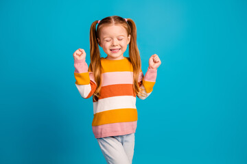 Happy young girl with colorful striped sweater posing with fists up against a blue background