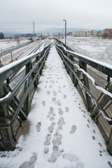Footprints on snowy pedestrian bridge crossing urban landscape