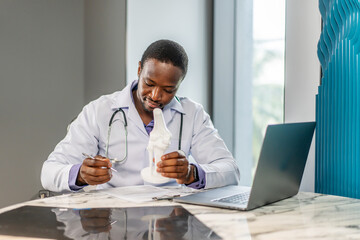 Male doctor is explaining something using an anatomical model bone while diagnosing bone density...