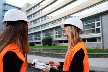 Female engineers wearing safety vests and hard hats, collaborating on a construction project with plans and charts