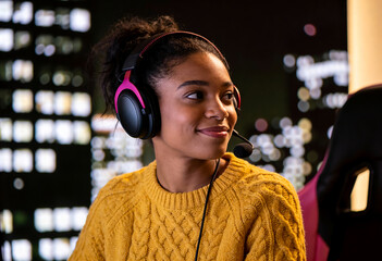 A woman wearing a yellow sweater and headphones is smiling. She is wearing a pink headset and is looking at the camera