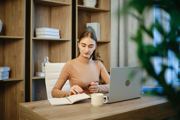 Woman sitting at desk working and writing with laptop in modern office space