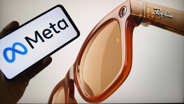 Hand holding smartphone with Meta logo next to Ray-Ban smart glasses