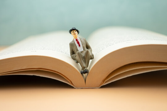 Small figure sits on open book with plain background and soft lighting during indoor scene