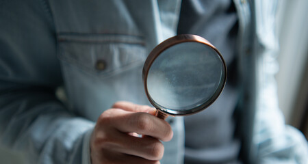 Hand holding a magnifying glass for search, investigation, and analysis concept. Discovery and inspection tool for business or research seo marketing trends