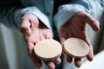 A person holding two blank circular wooden blocks in hands for graphic design, logo mockup, or text placement on a natural light background for creative crafts.
