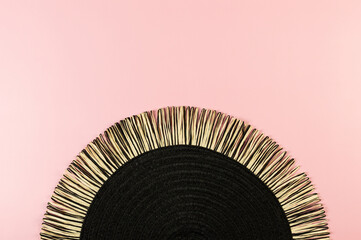 Top view of black wicker table mat on pink background. Straw round tray, flat lay, copy space. 