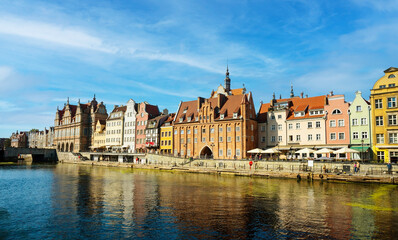 Fototapeta premium Charming historic architecture lines the waterfront of Gdansk under a clear blue sky. The river is bustling with boats, offering a vibrant scene with the city's iconic brick buildings