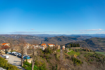 Naklejka premium Wide panoramic view of red tiled rooftops and rolling hills surrounding Motovun, Croatia, under clear daylight at winter 