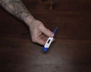 Male hand with tattoo holding medical thermometer over wooden table