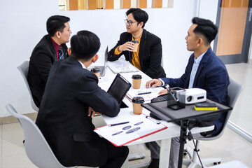 Group Of Businessmen In Professional Attire Engaged In Meeting Discussion Around Table With Laptops