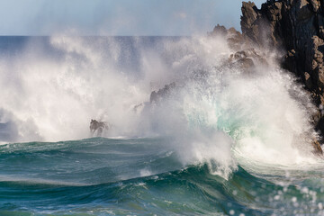 Waves crash against rocks at the mainland's easternmost point, creating rainbows in the ocean spray. Daylight, Byron Bay, New South Wales, Australia.