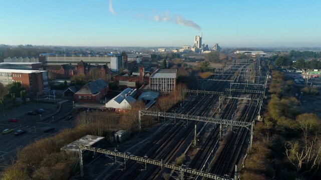 Aerial view of mainline train railway tracks in central Rugby, industrial factories and large cement plant in background, sunny winter day UK