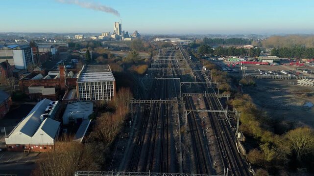 Aerial view of mainline train railway tracks in central Rugby, industrial factories and large cement plant in background, sunny winter day UK