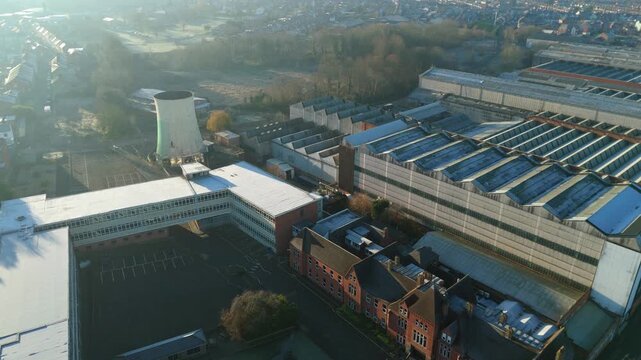 Aerial view of industrial factory complex with small cooling tower and textured rooftops in bright winter sunshine, Rugby UK