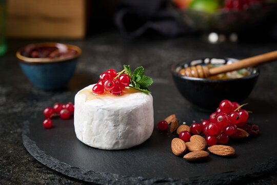 Sliced ​​Camembert dessert cheese on a stone plate with red currants, almond nut and fruit.