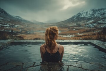 Woman enjoys hot spring with mountains in background during cloudy day