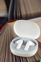 Small white headphones against a background of many books. Audiobook concept