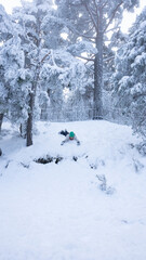Child sliding down snowy hill in winter forest