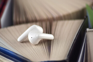 Small white headphones against a background of many books. Audiobook concept