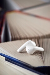 Small white headphones against a background of many books. Audiobook concept