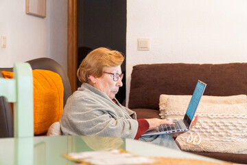 Senior woman at home enjoying using the laptop sitting on a armchair