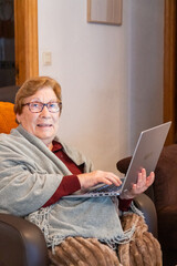 Senior woman at home enjoying using the laptop sitting on a armchair