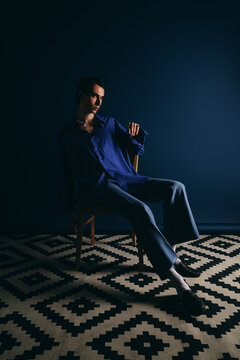 Stylish man in elegant blue attire seated on chair against dark backdrop