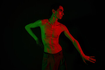 Stylish man poses dramatically in vibrant green and red lighting against a dark backdrop