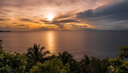 Dramatic sunset over calm ocean waters with clouds and tropical foliage