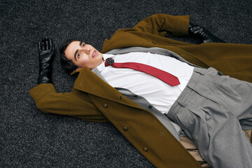 Stylish man in a fashionable outfit lies on textured flooring with a casual demeanor