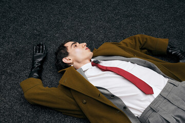 Stylish man lies gracefully on floor dressed in chic fashion with striking red tie and gloves